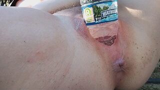 A busty MILF pees in a bottle and masturbates outdoors, showcasing her gape